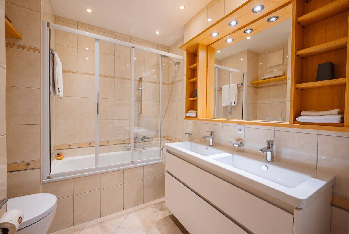 Modernes Badezimmer mit beigen Fliesen, Dusch-Badewanne, Doppelwaschbecken und Spiegelschrank.