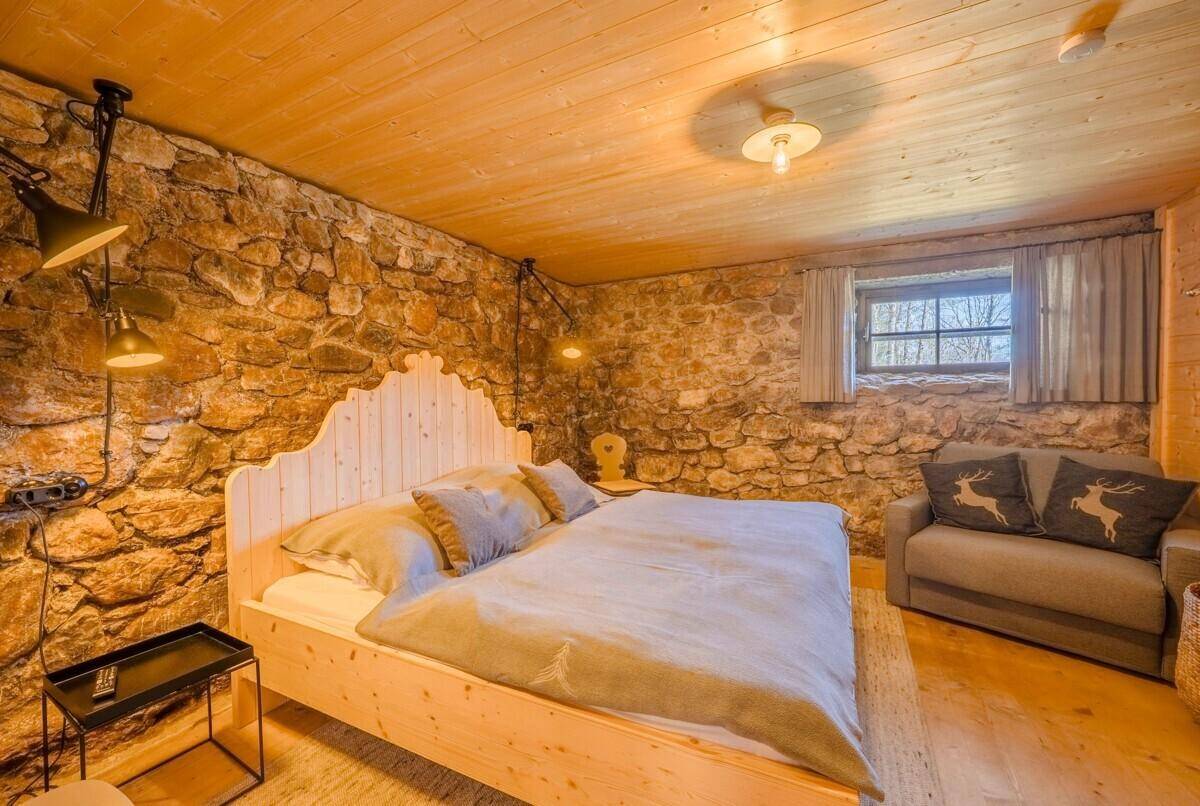 Rustikales Schlafzimmer mit Steinwänden, Holzboden und einem gemütlichen Doppelbett.