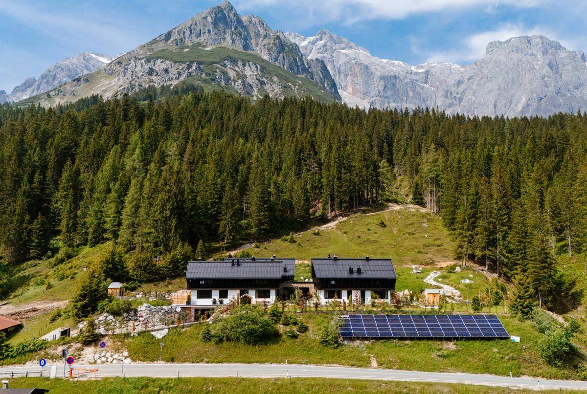 Zwei moderne Chalets in alpiner Landschaft mit Photovoltaikanlage und Wald.