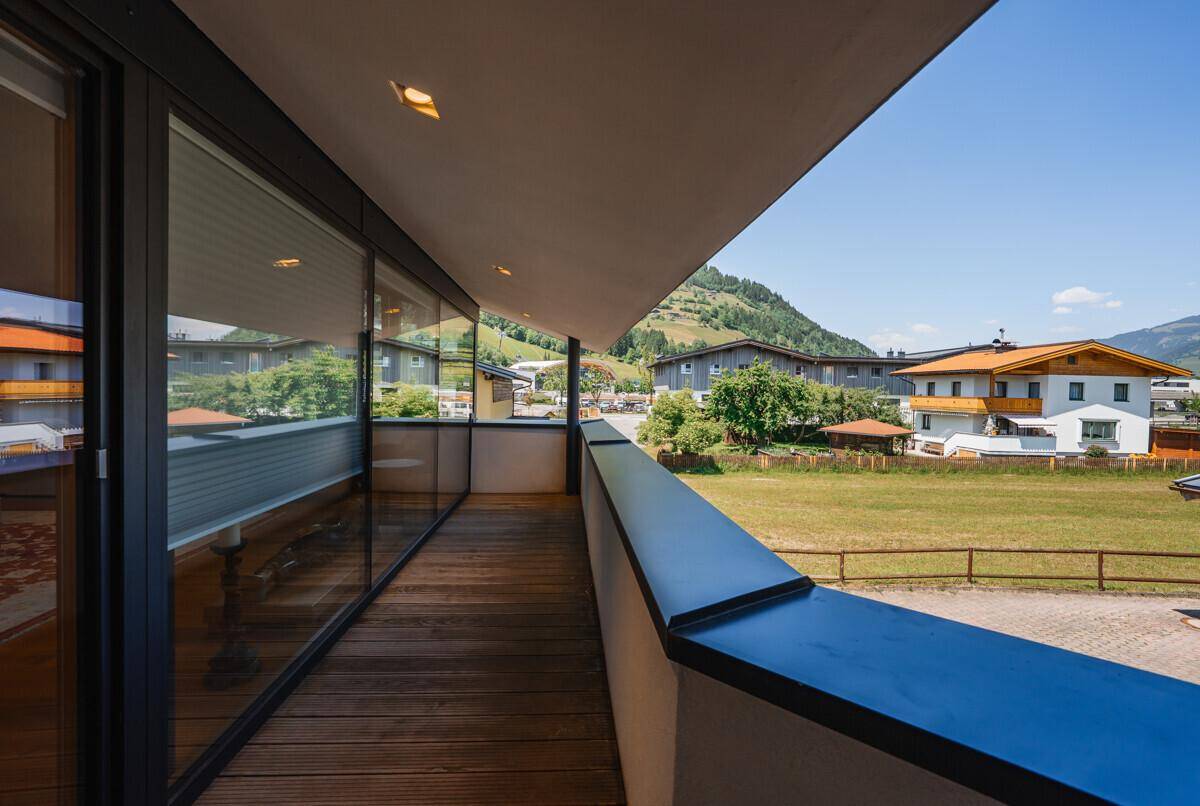 Langer Balkon mit Holzboden und Glasgeländer, bietet weite Aussicht auf die Umgebung.