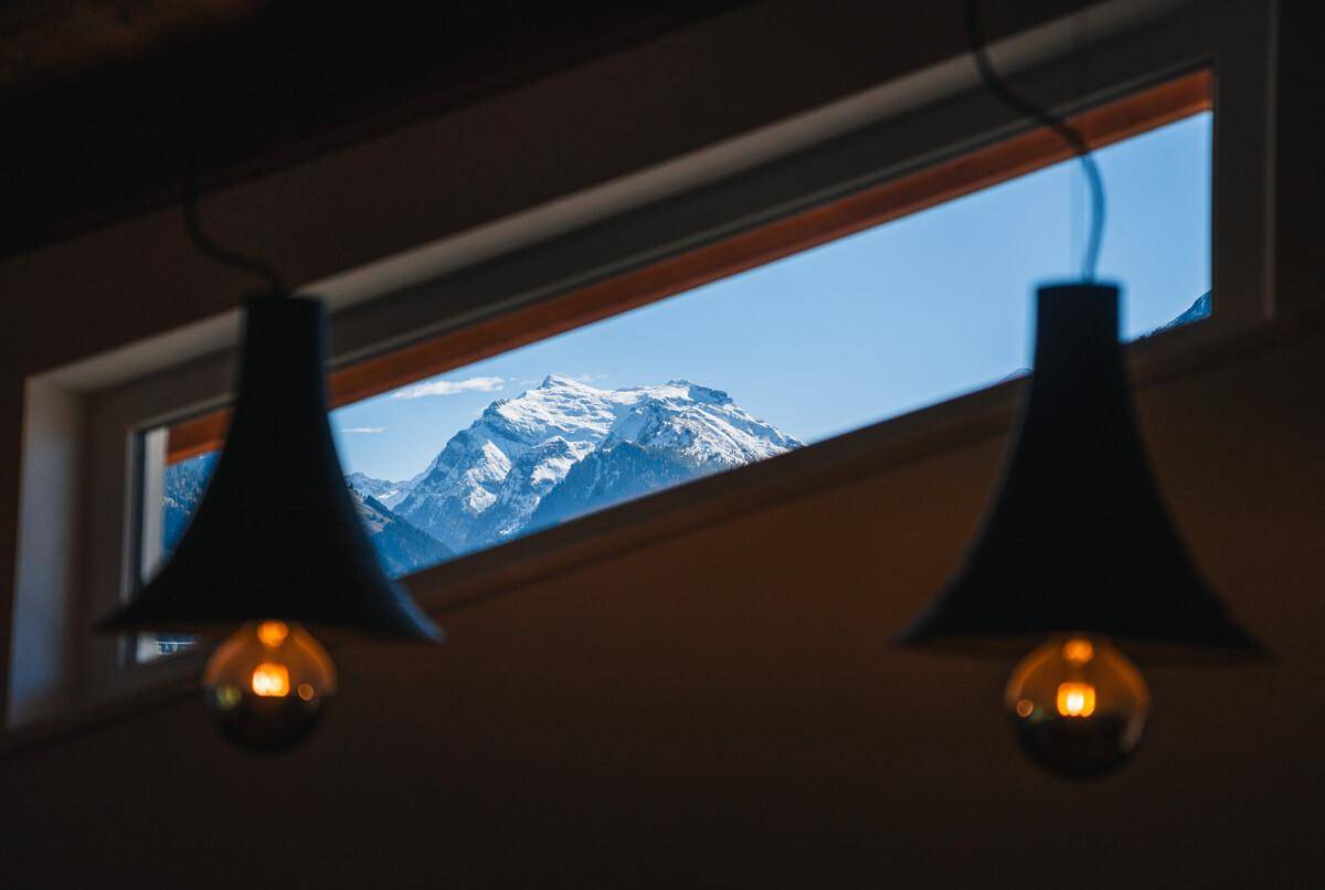Fenster mit beeindruckendem Blick auf schneebedeckte Berge und dunkle Hängelampen im Vordergrund.