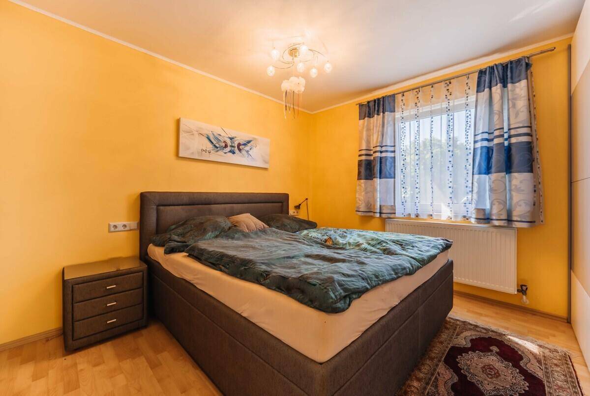 Schlafzimmer mit gelben Wänden, Doppelbett und einem Fenster mit gemusterten Vorhängen.
