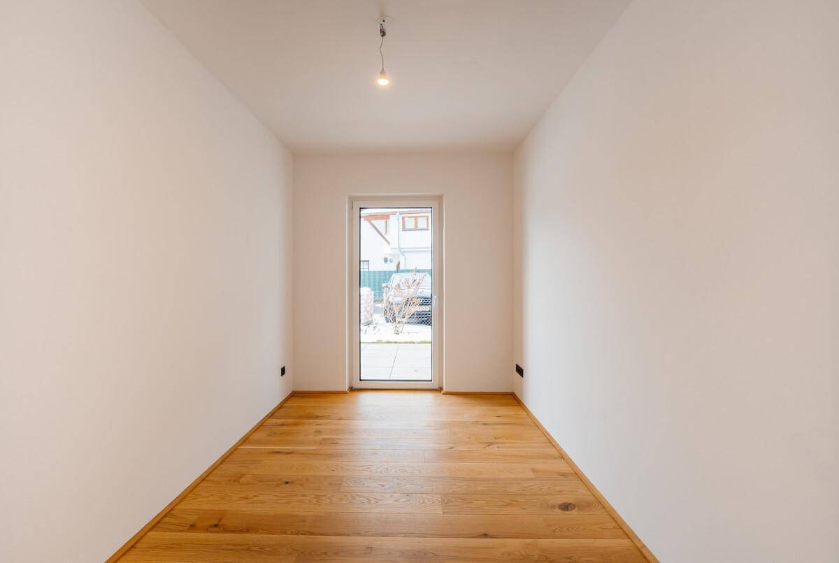 Helles, leeres Zimmer mit Holzboden und Fensterblick ins Grüne, vielseitig nutzbar.