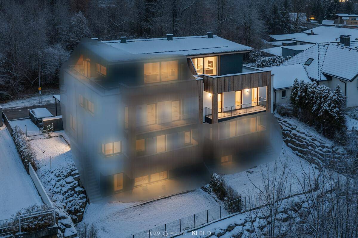 Modernes Mehrfamilienhaus in winterlicher Landschaft mit beleuchteten Balkonen und Terrassen.