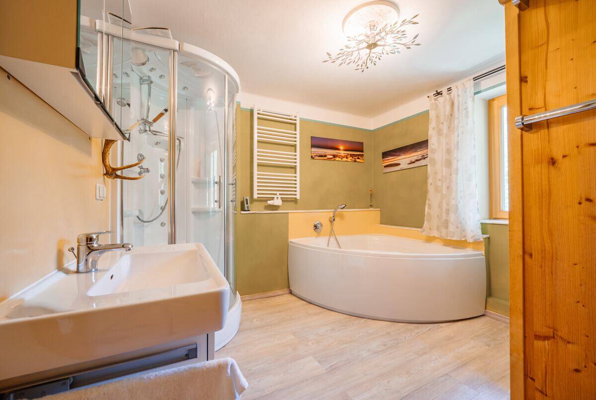 Geräumiges Badezimmer mit Badewanne, Duschkabine, Waschbecken und beheiztem Handtuchhalter.