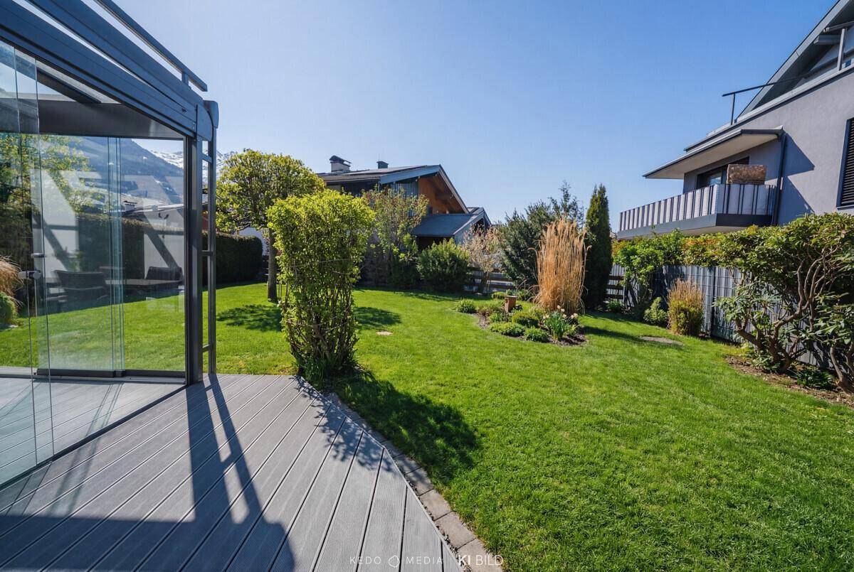 Gepflegter Garten mit Rasenfläche, Sträuchern und direktem Zugang zum Wintergarten des Hauses.