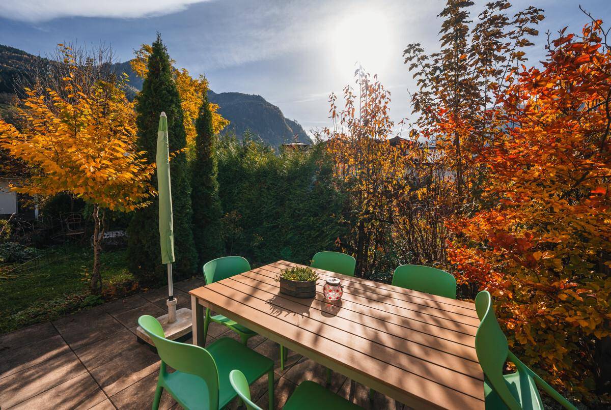 Geräumige Terrasse mit Esstisch und Stühlen, umgeben von herbstlicher Vegetation und Bäumen.