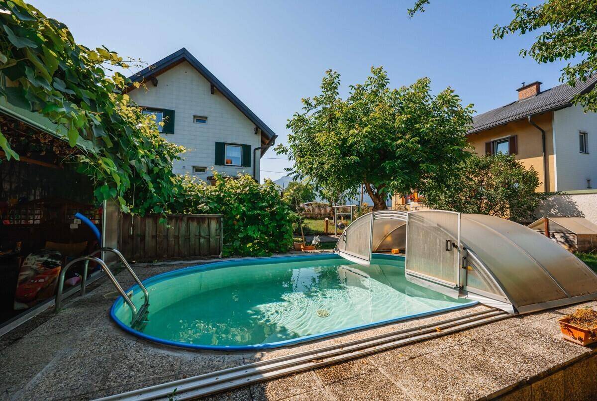 Außenpool mit Schiebeabdeckung im Garten, umgeben von Grünflächen und Wohnhäusern.