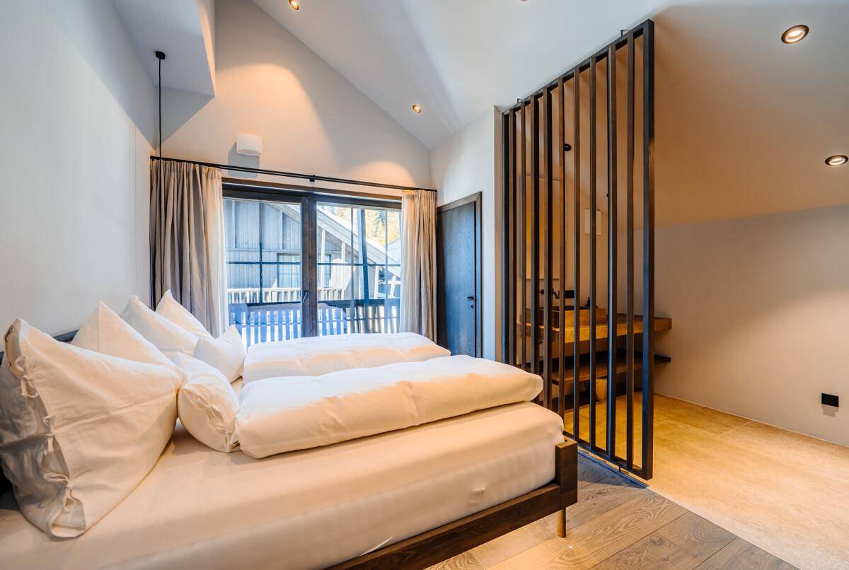 Helles Schlafzimmer mit Holzboden, Dachschräge und offenem Zugang zum Badezimmerbereich.