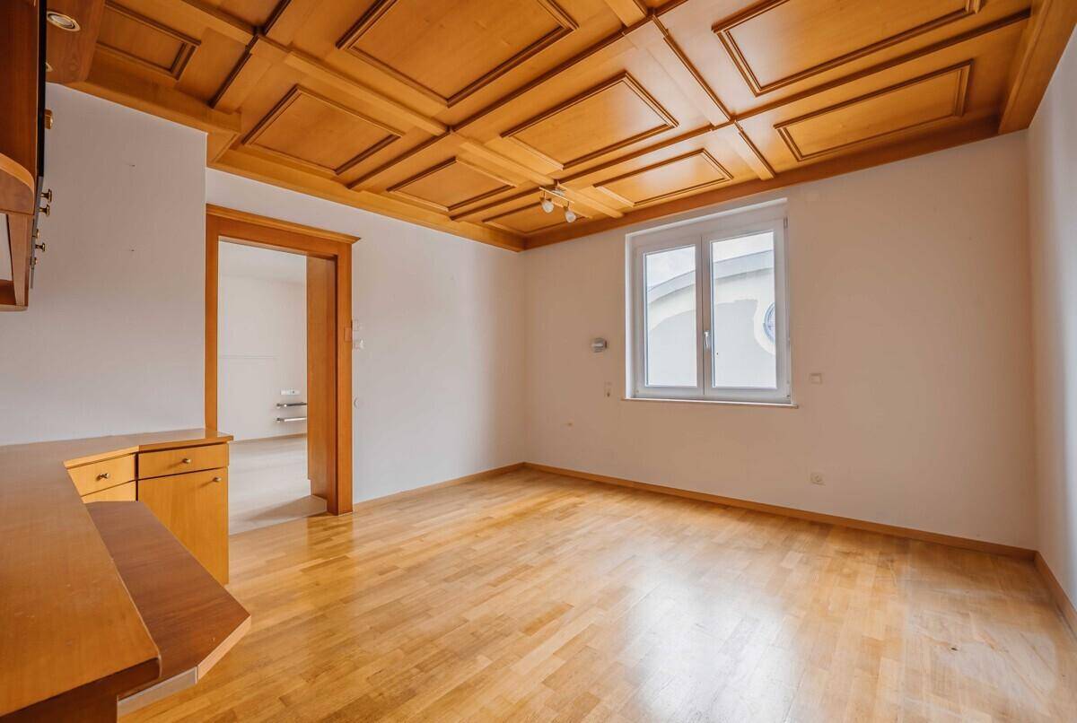 Geräumiges Zimmer mit Holzkassettendecke, Parkettboden und einem großen Fenster.