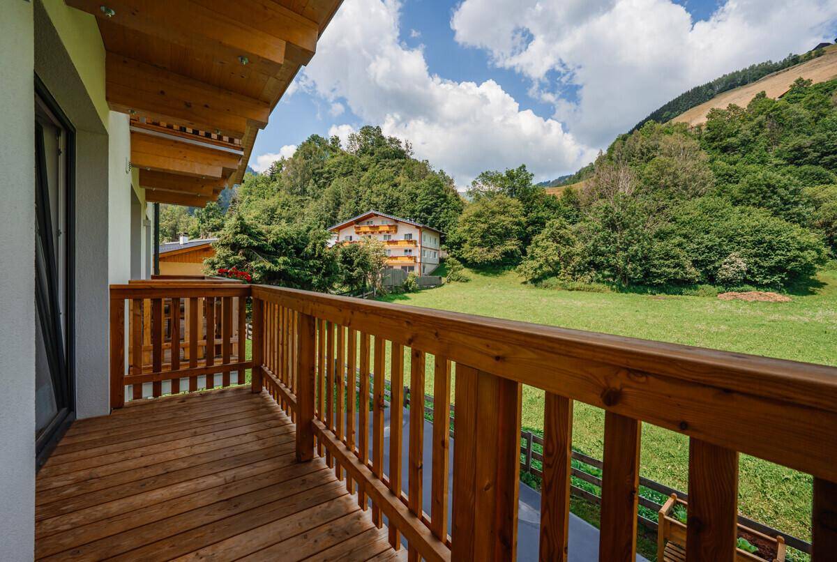 Balkon mit Holzgeländer und Blick auf die grüne Hügellandschaft und umliegende Natur.