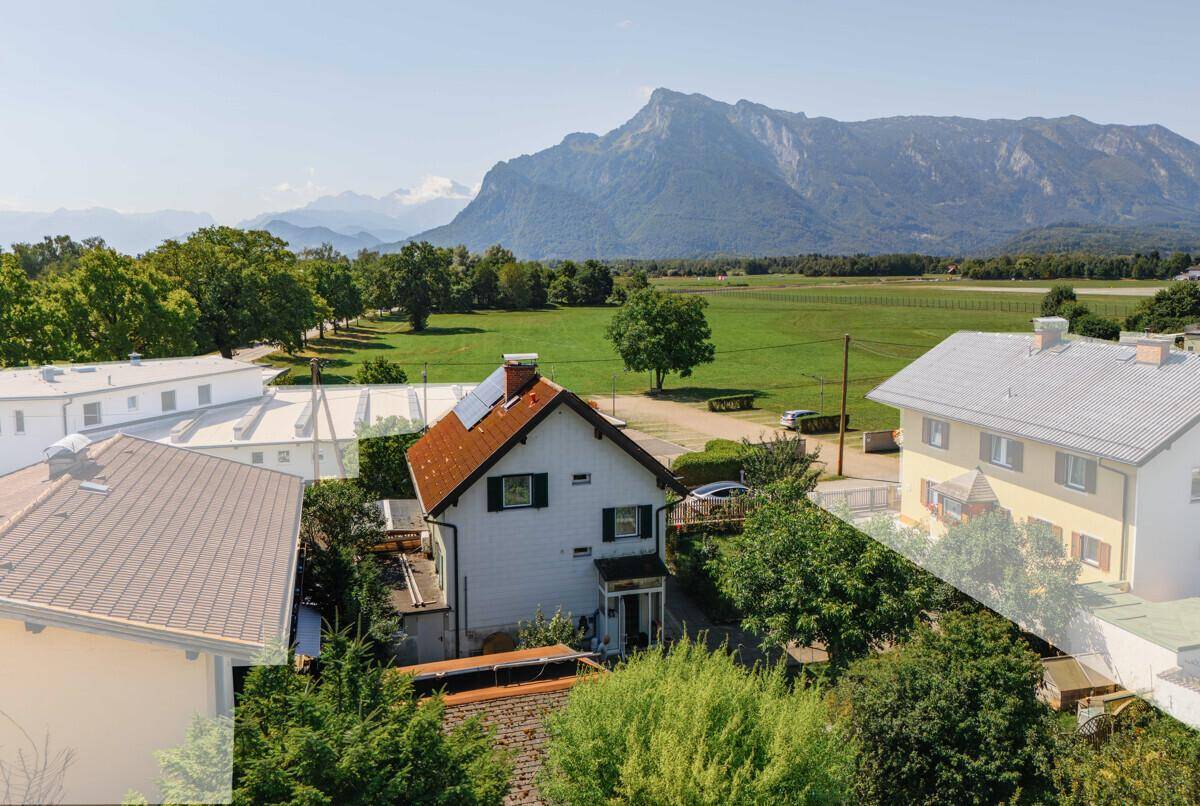 Wohnhaus mit Solaranlage und weitem Blick auf grüne Felder und majestätische Berge im Hintergrund.