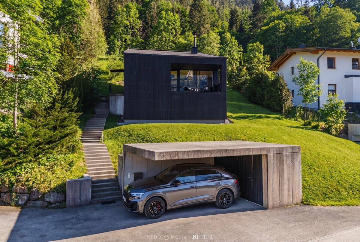 Modernes Haus mit schwarzer Holzfassade, Carport und Treppe im Grünen, eingebettet in die Natur.