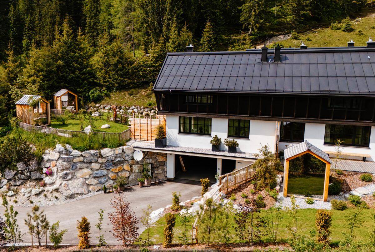 Modernes Gebäude in alpiner Landschaft mit gepflegtem Garten und Zufahrt.