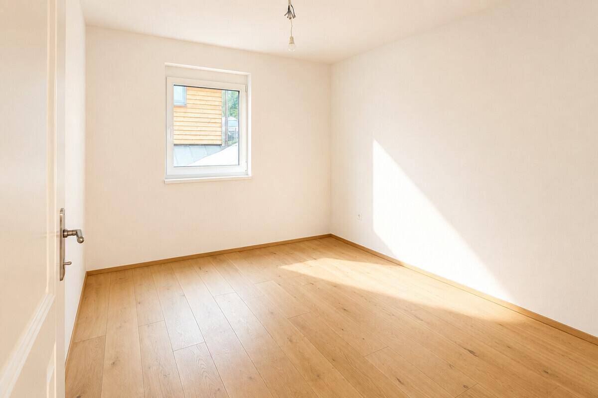 Helles, leeres Zimmer mit Holzboden und Fenster, ideal als Schlaf- oder Gästezimmer.