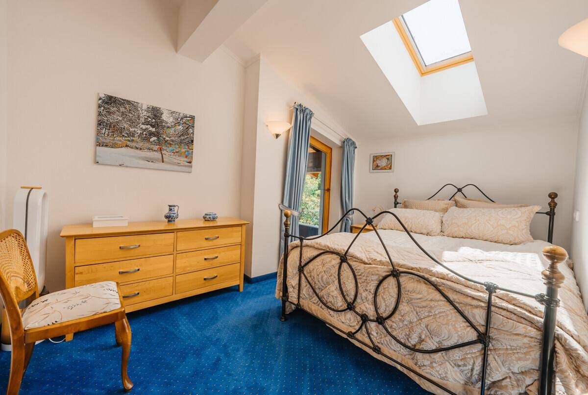 Gemütliches Schlafzimmer mit schmiedeeisernem Bett, blauer Teppichboden und Dachfenster.