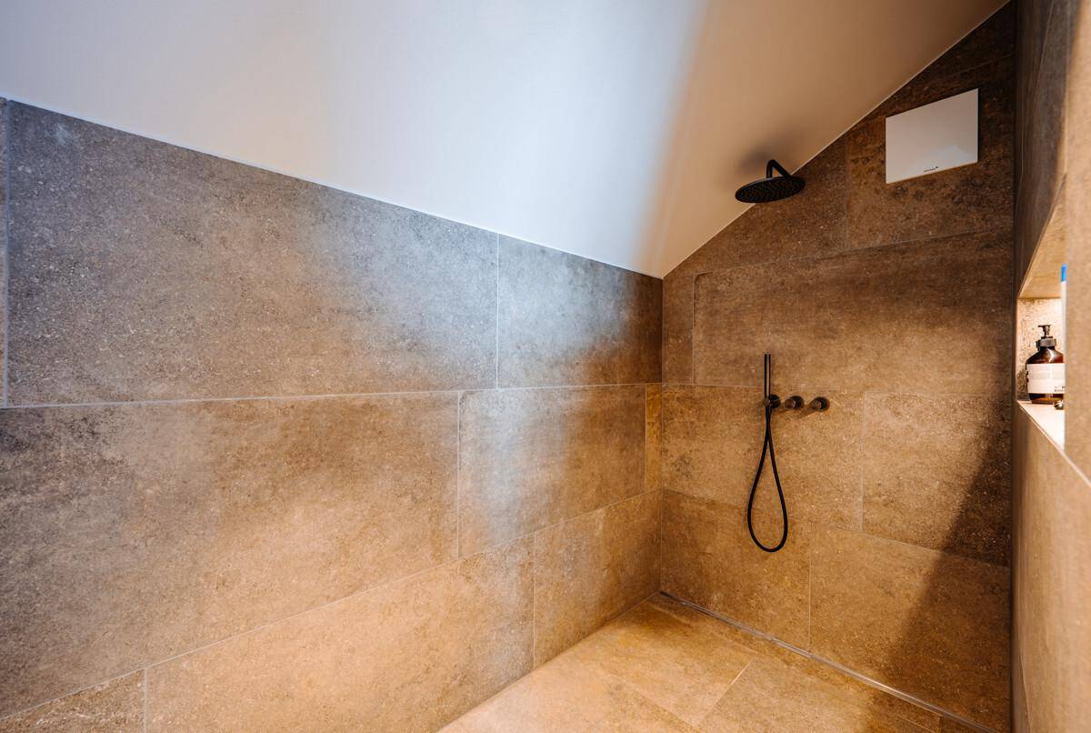 Moderne Dusche mit großformatigen Fliesen und Regenduschkopf in schräger Dachschräge.