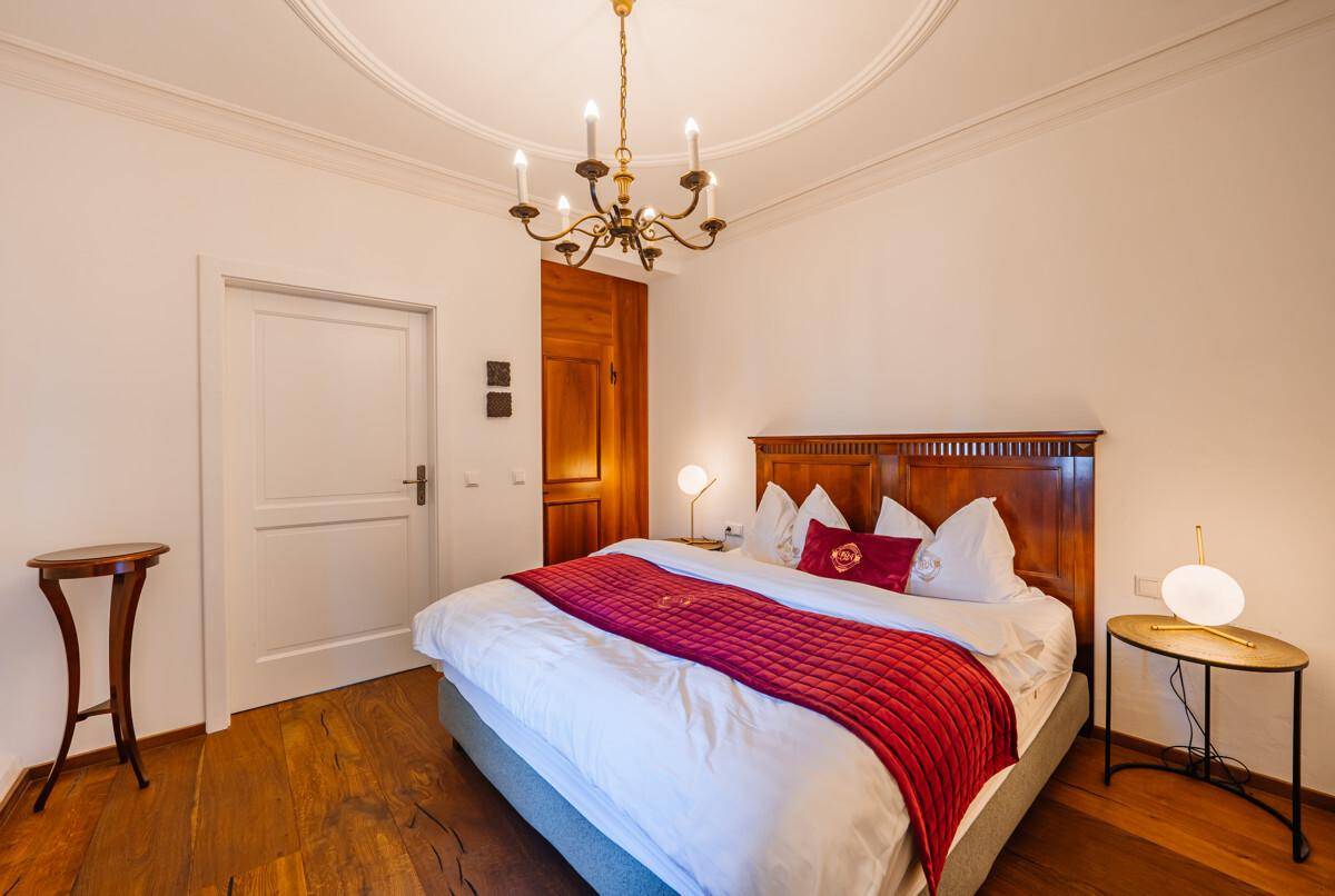 Schlafzimmer mit großem Holzbett, Holzboden, Stuckdecke und traditionellem Kronleuchter.