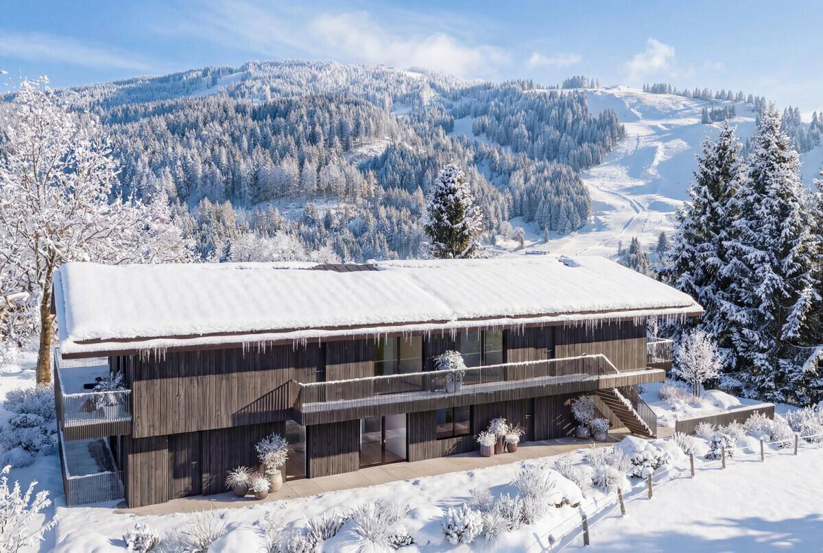 Modernes Gebäude im Winter am Tag, umgeben von verschneiten Bäumen und Hügeln.