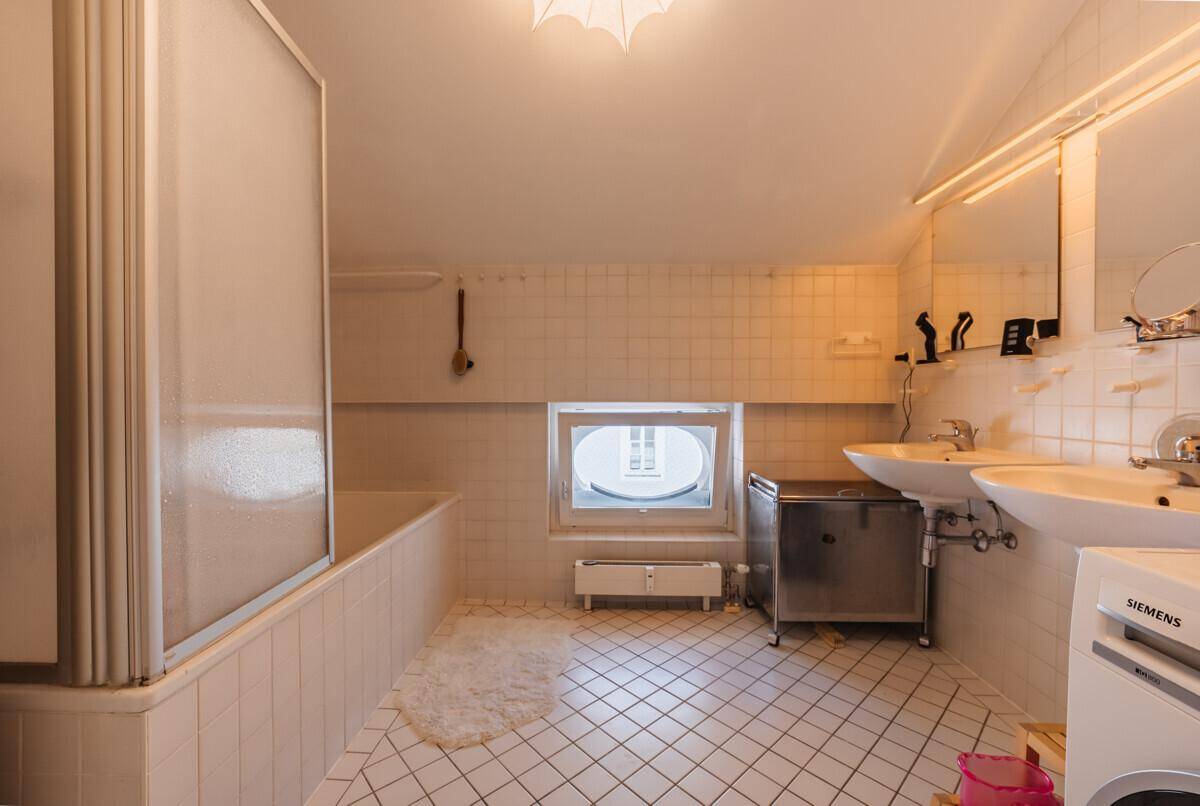 Funktionales Badezimmer mit weißen Fliesen, Doppelwaschbecken und Badewanne mit Duschwand.