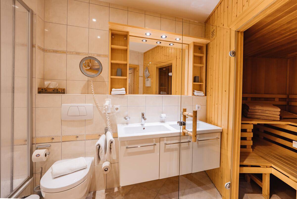 Badezimmer mit Dusche, Doppelwaschbecken, Toilette und integrierter Sauna.