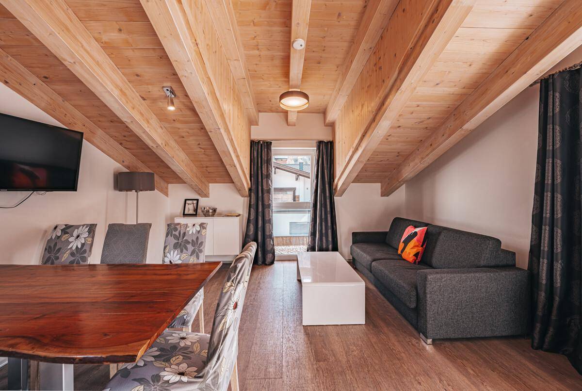 Gemütlicher Wohn- und Essbereich mit Holzbalkendecke, Sofa und großem Esstisch.