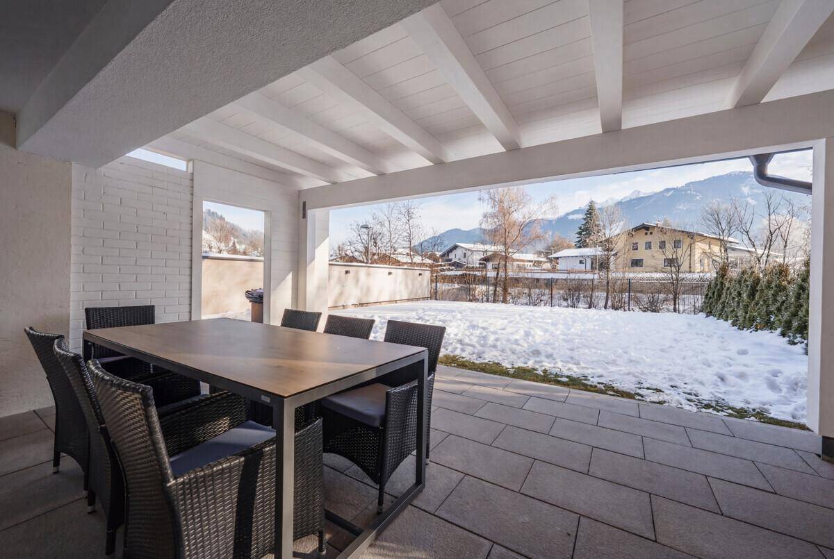 Überdachte Terrasse mit Esstisch und Blick auf den verschneiten Garten und die Berge.