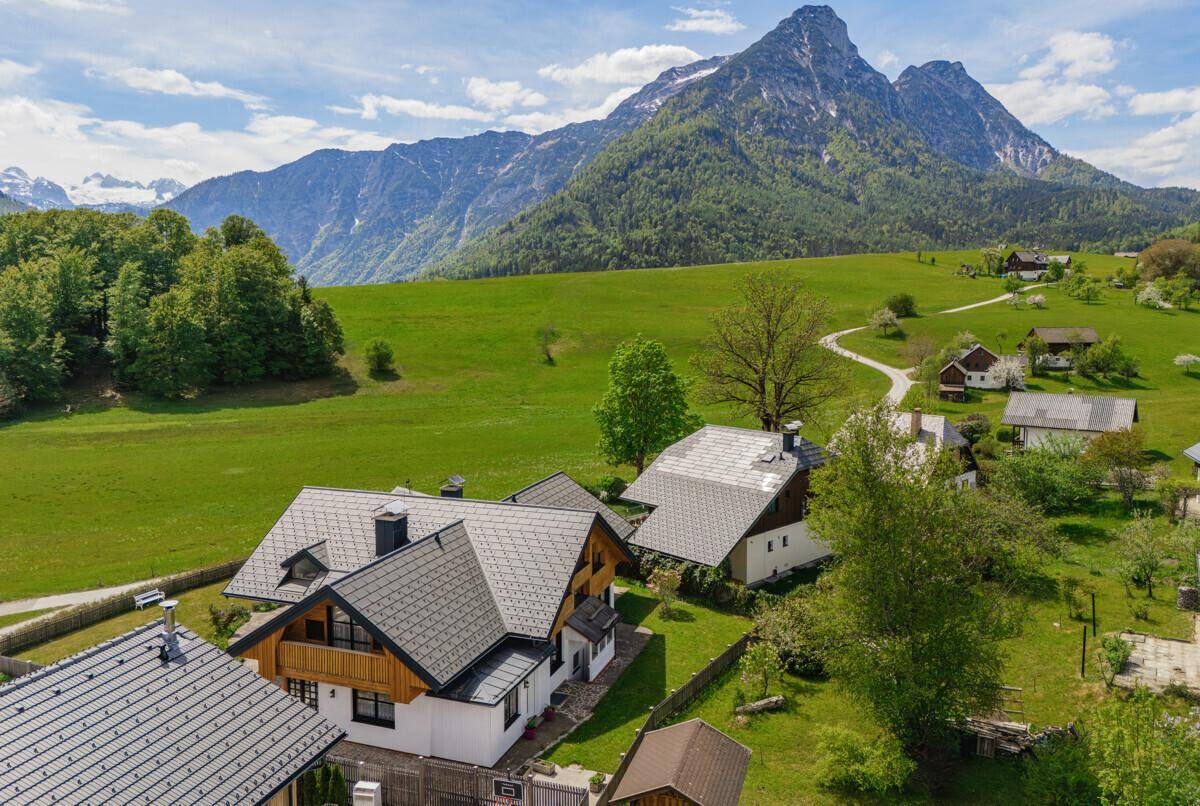 Panoramablick auf das Landhaus in den Bergen, umgeben von grünen Wiesen und Bäumen.