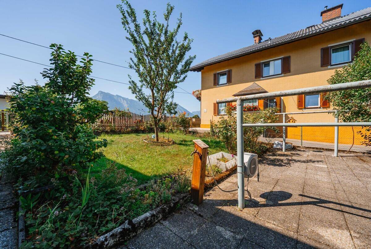 Sonniger Gartenbereich mit Rasenfläche, Obstbäumen und einer Terrasse vor dem Wohnhaus.