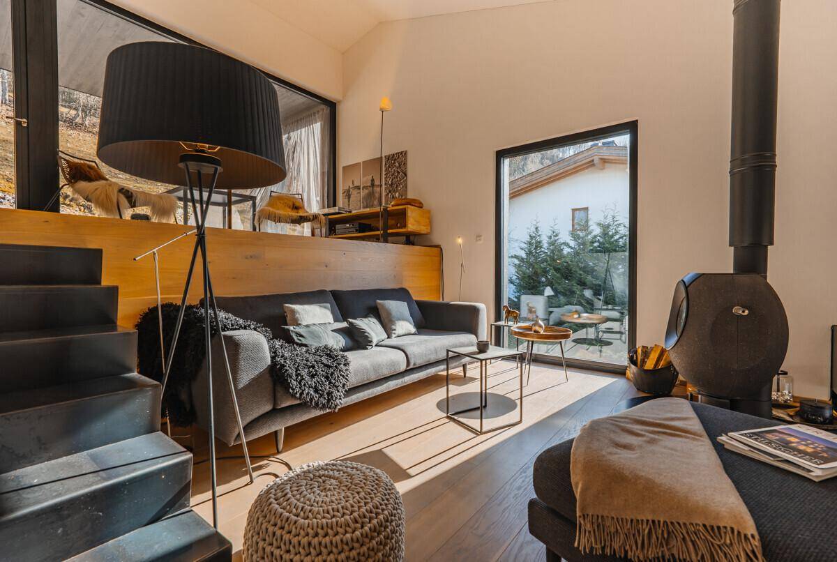 Gemütliches Wohnzimmer mit Sofa, Holzboden und modernem Kaminofen, lichtdurchflutet und einladend.