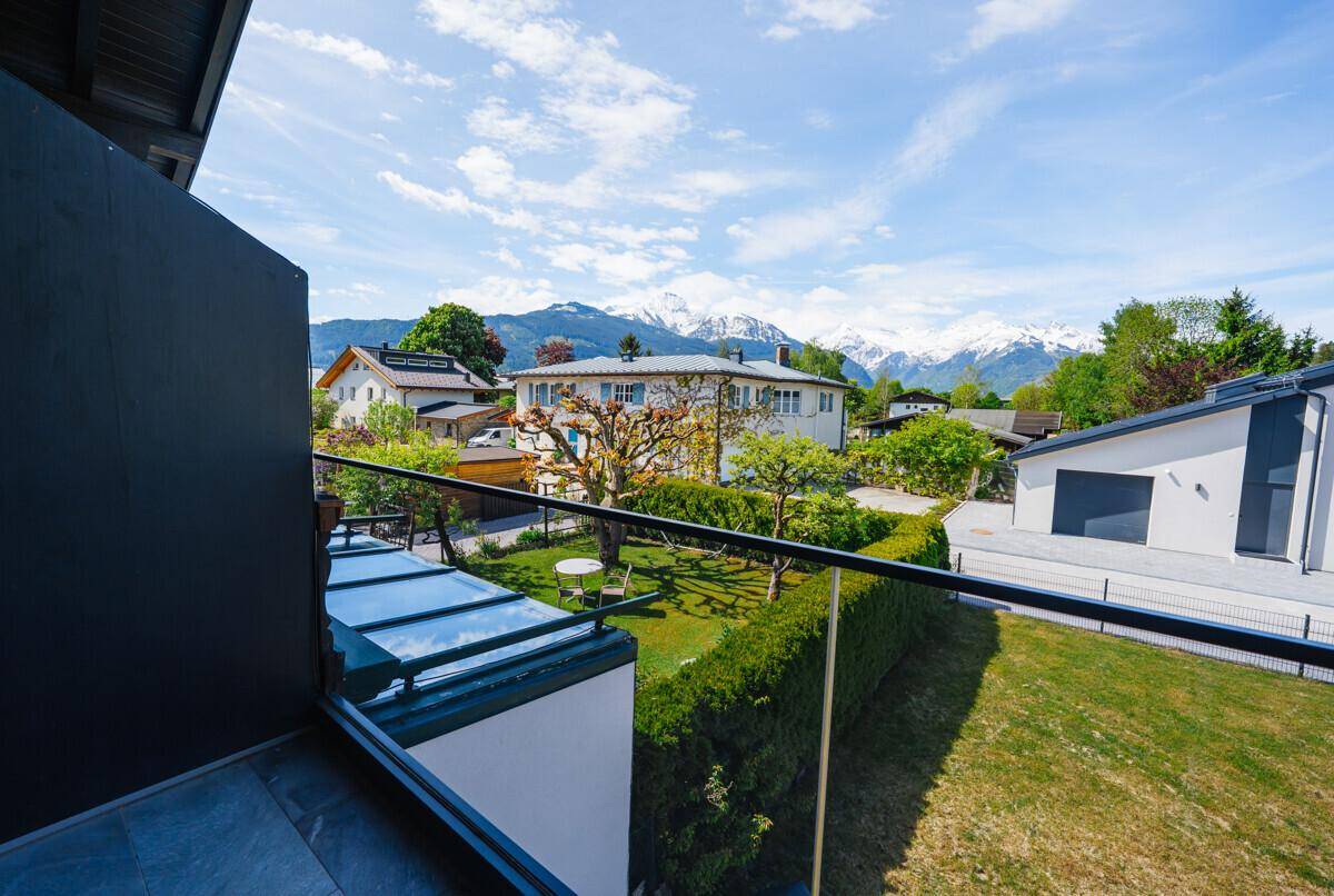 Balkon mit Glasgeländer, Blick auf den Garten und die umliegende Berglandschaft.