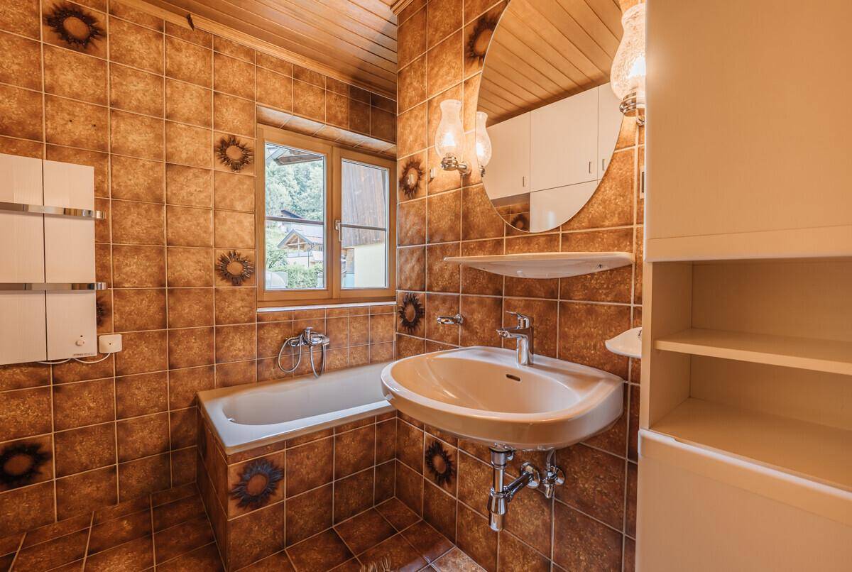 Badezimmer mit braunen Fliesen, Badewanne und Fenster, im traditionellen Stil gehalten.