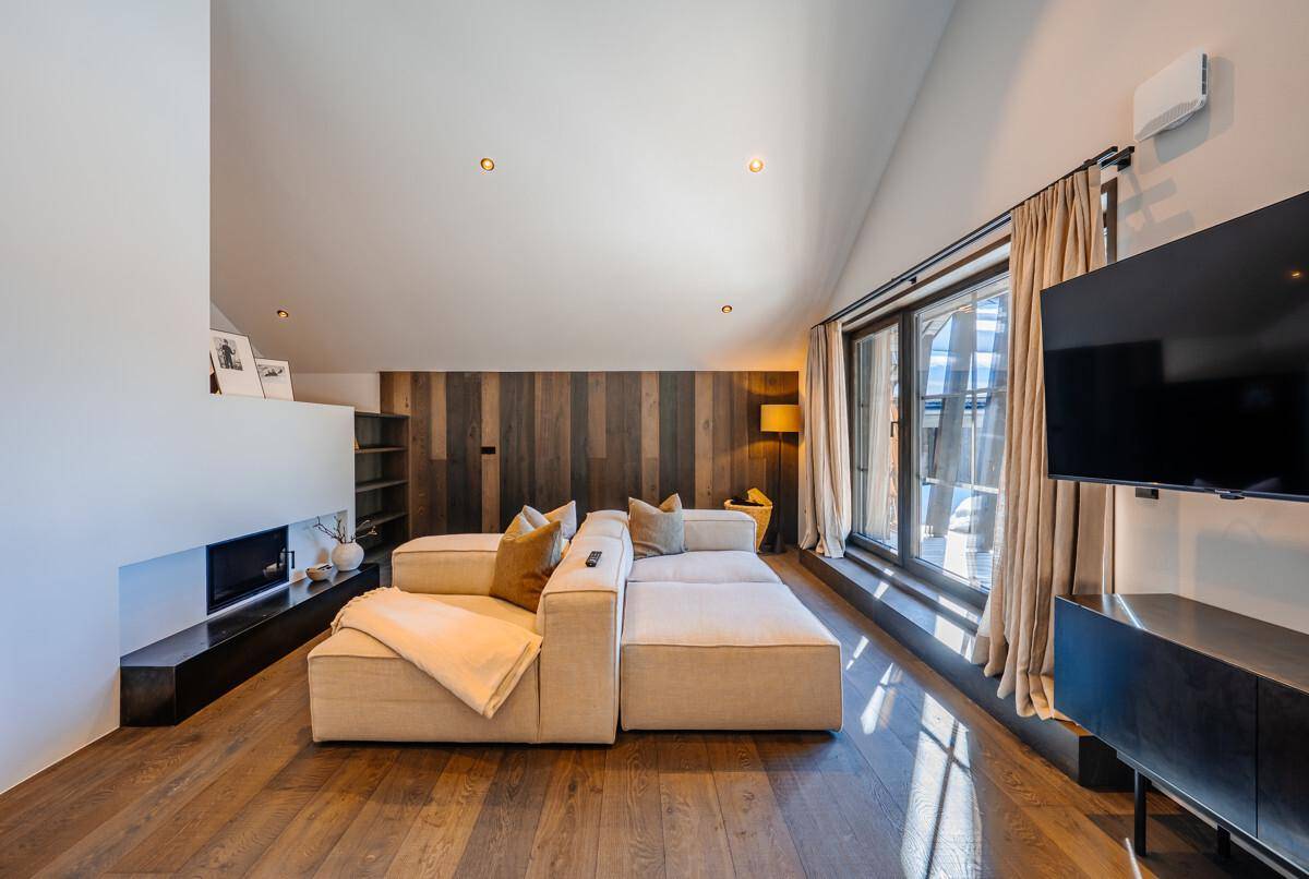 Gemütliches Wohnzimmer mit Holzboden, modernem Sofa und Kamin in alpiner Umgebung.