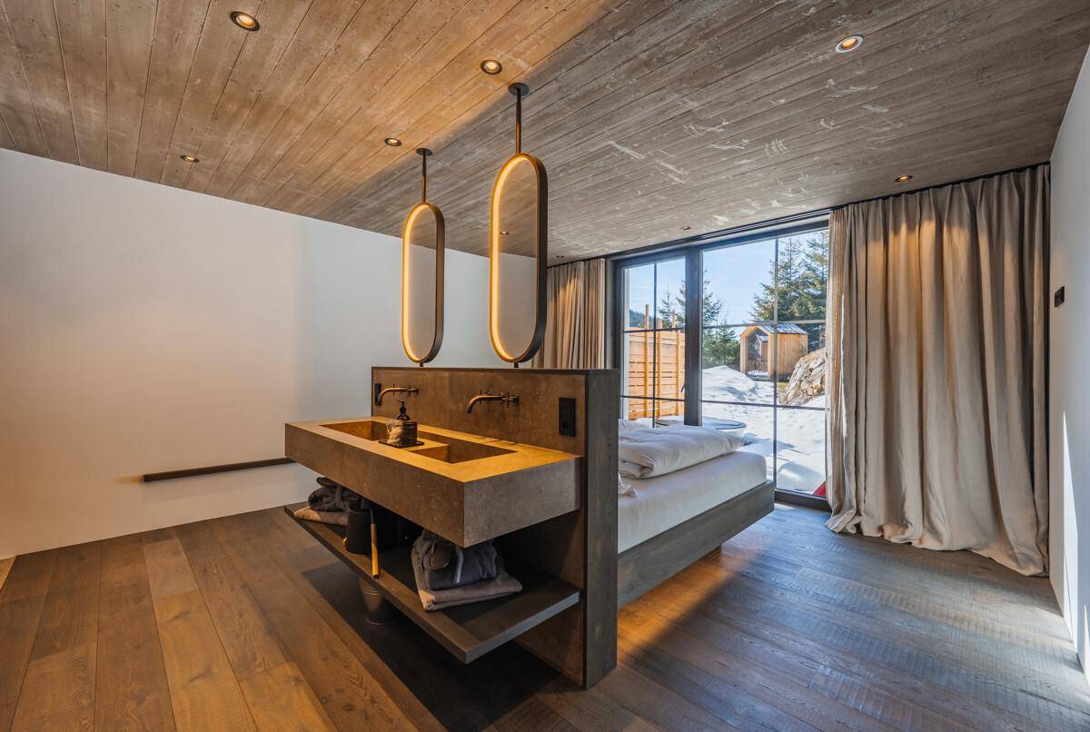 Modernes Schlafzimmer mit Doppelbett, Holzboden und offenem Badbereich mit Doppelwaschbecken.