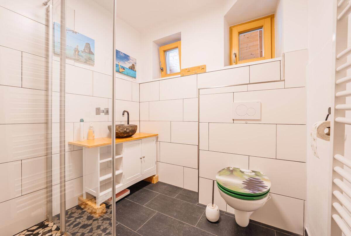 Modernes Badezimmer mit weißen Fliesen, begehbarer Dusche und wandhängendem WC.