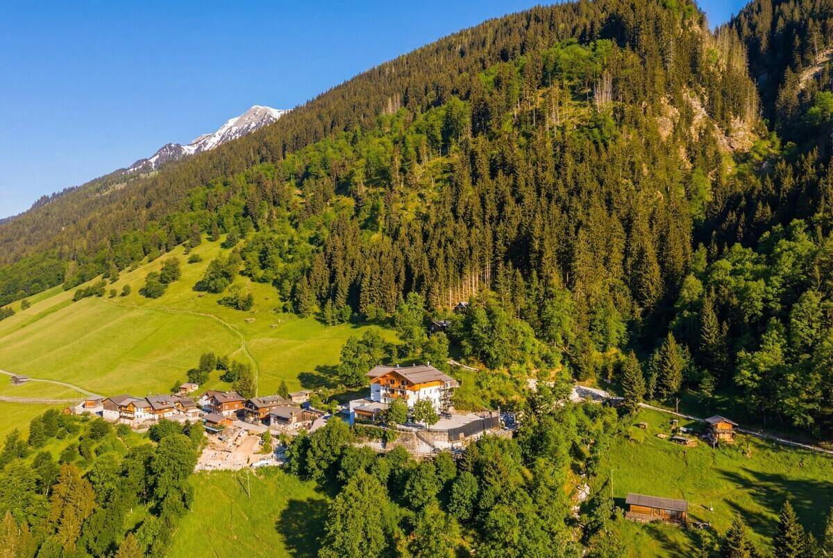 Weitläufige Luftaufnahme eines Gebäudes in den Bergen, umgeben von grünen Wäldern und Wiesen.