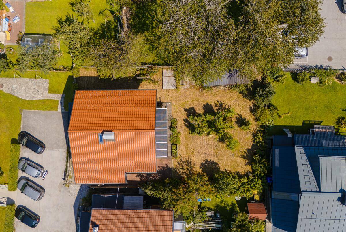 Luftaufnahme eines Hauses mit rotem Ziegeldach, Garten und Parkplätzen.