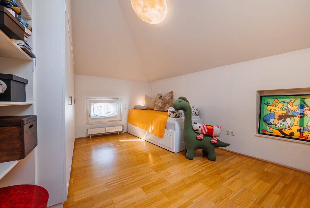 Helles Kinderzimmer mit Holzboden, Einbauregalen und schrägem Dach.