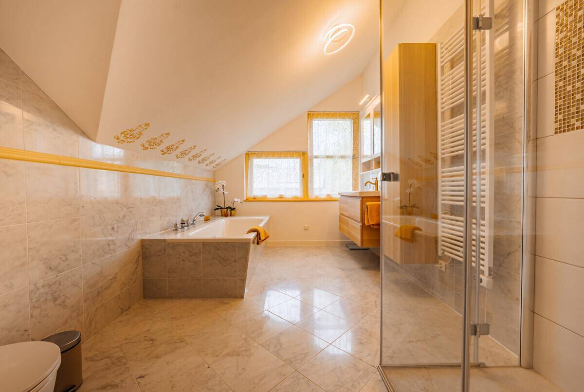 Helles Badezimmer mit Badewanne, Dusche, Marmorfliesen und Dachschräge.