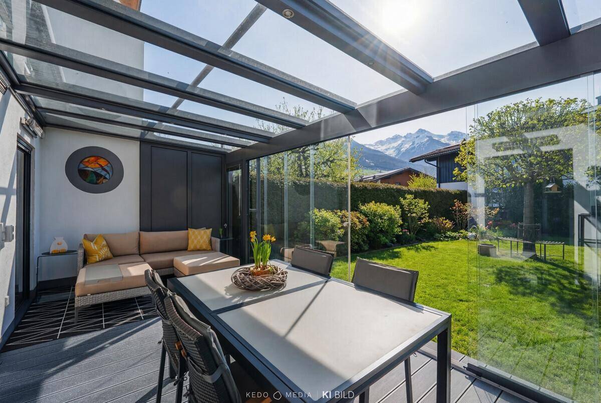Heller Wintergarten mit Sitzgelegenheiten, Esstisch und Panoramablick auf die umliegenden Berge.