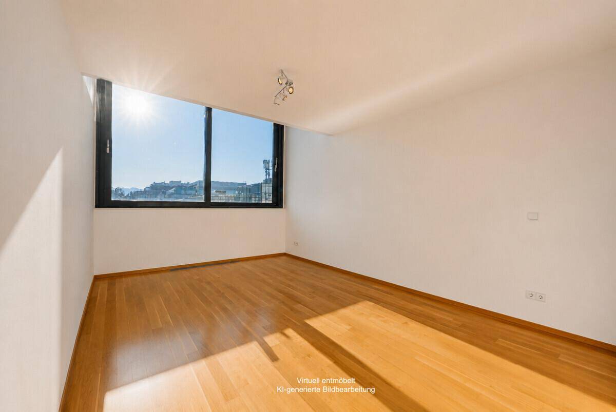Heller, unmöblierter Raum mit Holzboden und großem Fenster, das viel Sonnenlicht hereinlässt.