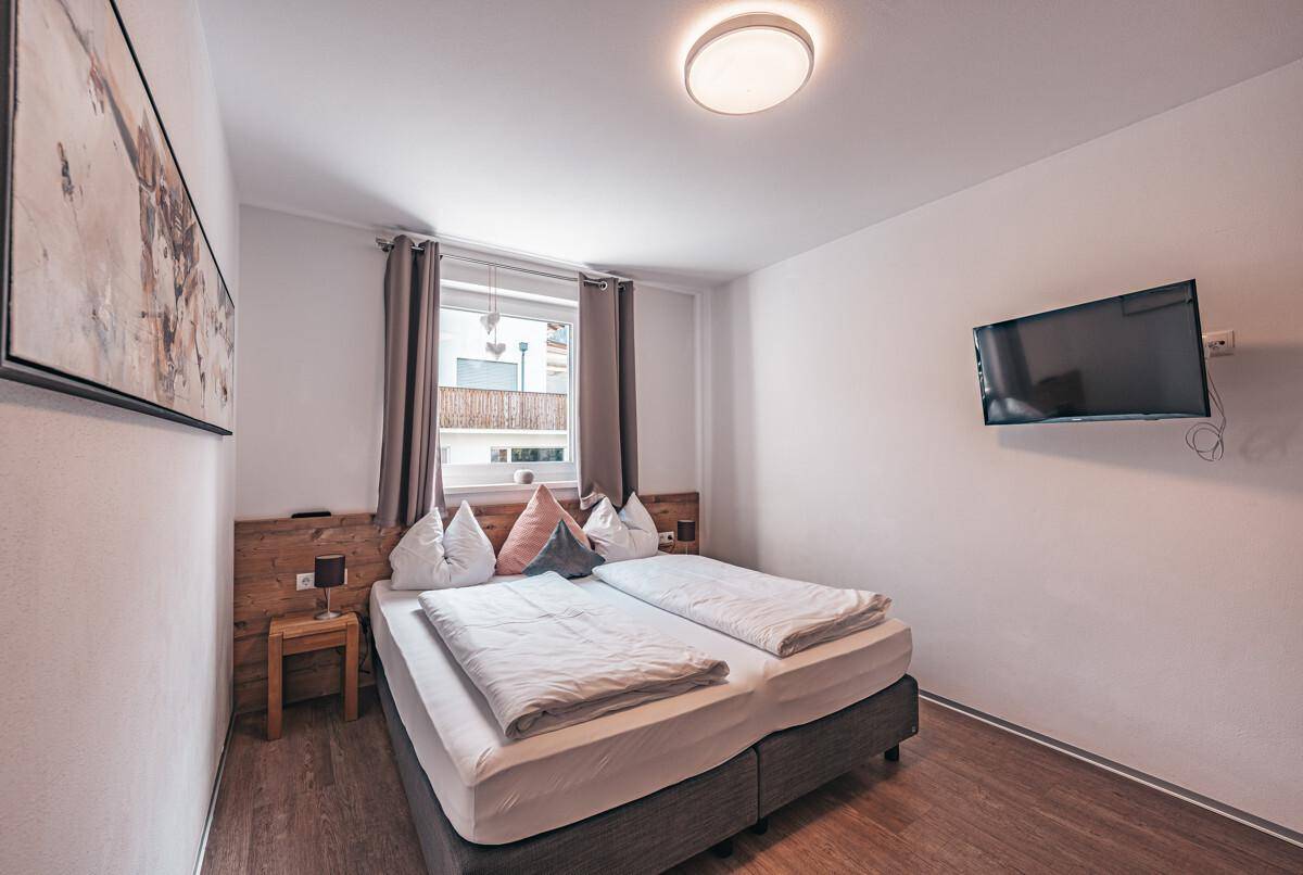 Helles Schlafzimmer mit Doppelbett, Holzkopfteil und einem Fenster mit Blick nach draußen.