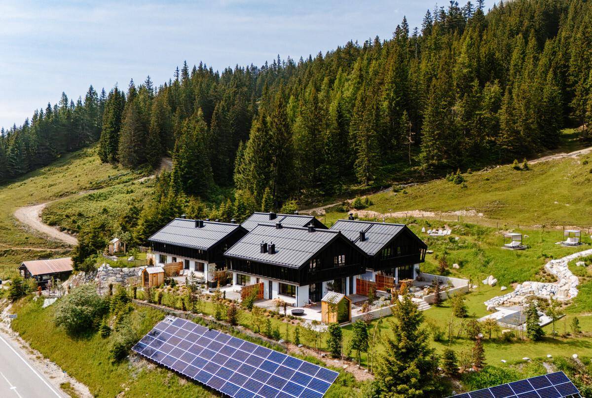Luftaufnahme von mehreren modernen Gebäuden in einer grünen Berglandschaft mit Solaranlagen.