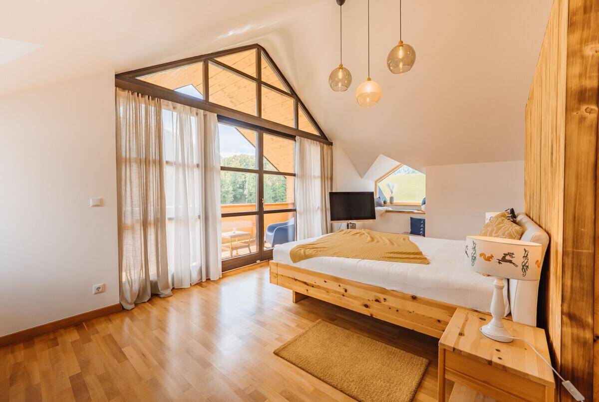 Helles Schlafzimmer mit Holzboden, großen Fenstern und Zugang zu einem Balkon mit Bergblick.
