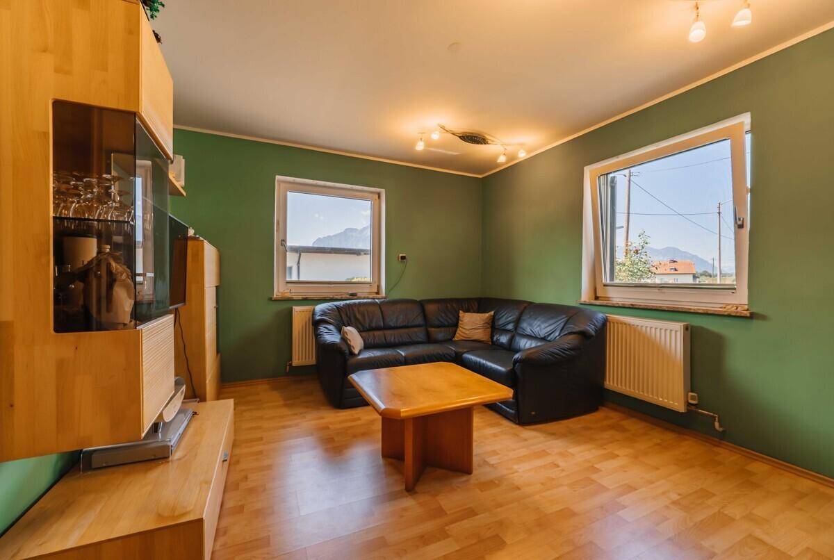 Helles Wohnzimmer mit grünen Wänden, Laminatboden und einer bequemen Ledercouch.