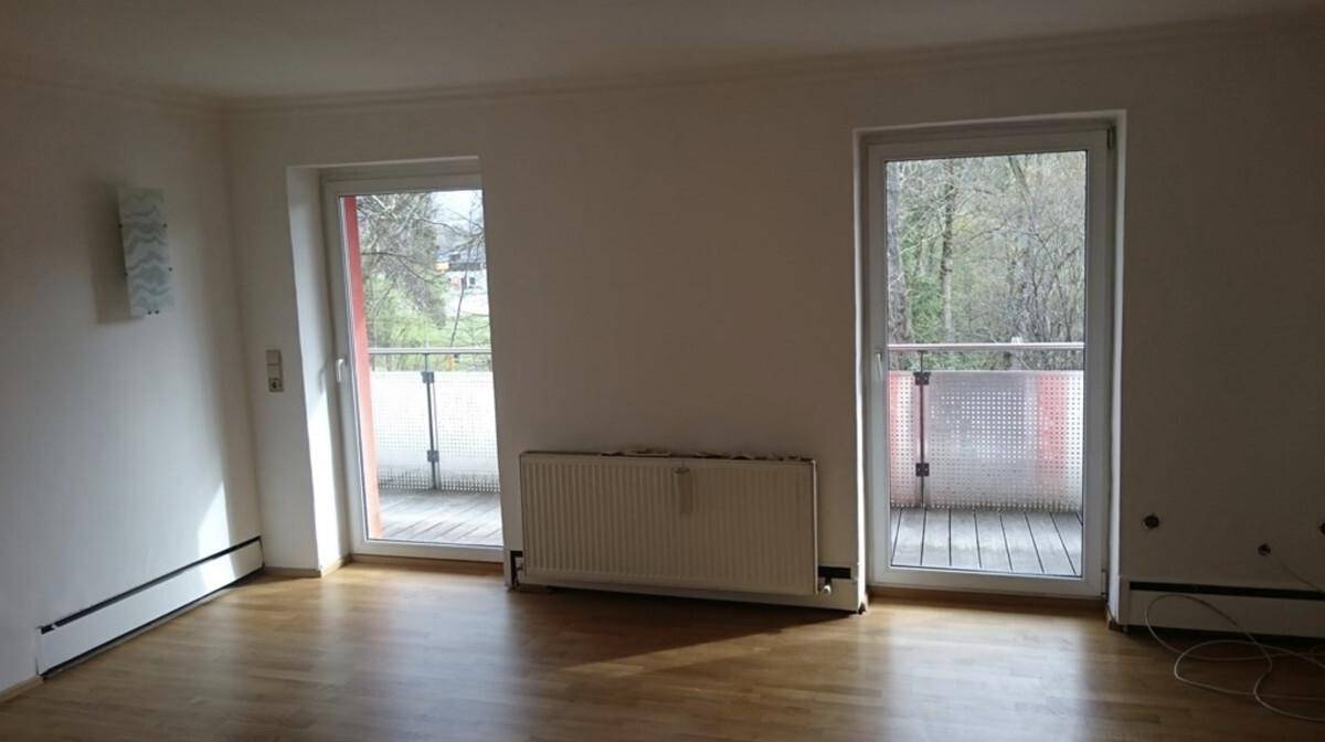 Helles Wohnzimmer mit Holzboden und zwei Zugängen zu französischen Balkonen.