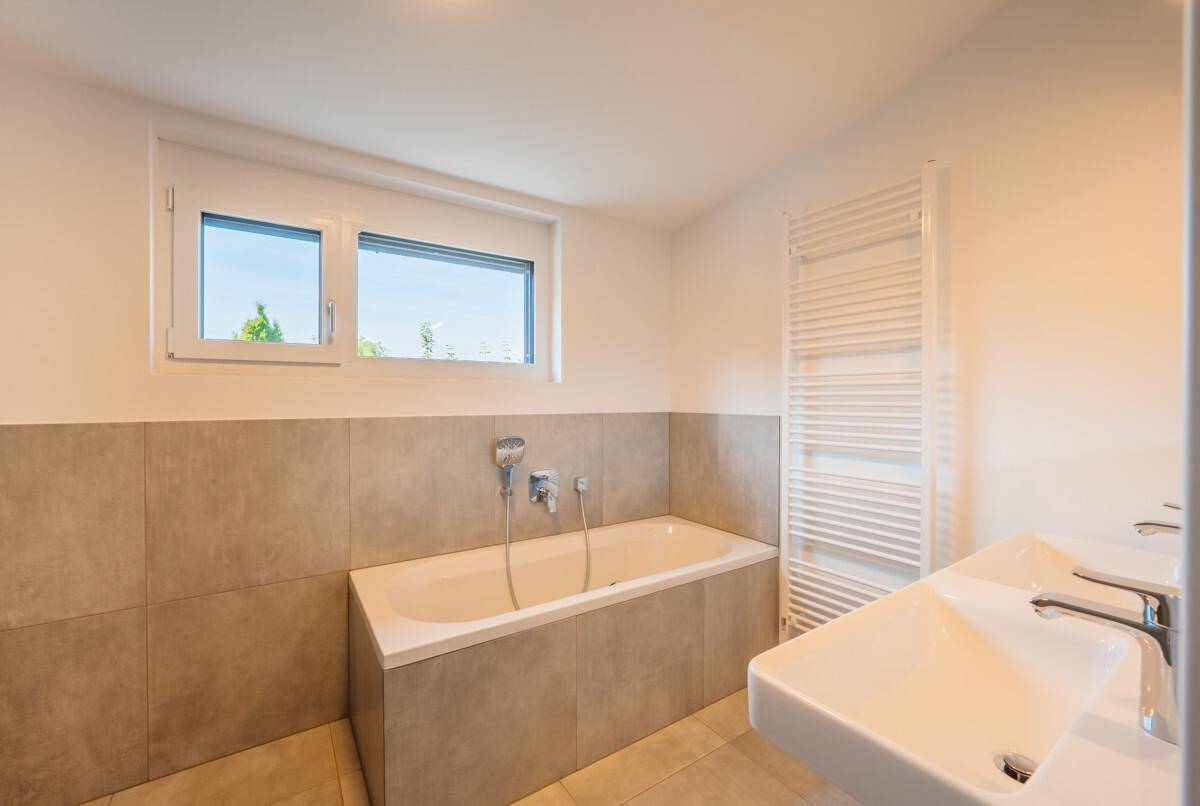 Modernes Badezimmer mit Badewanne, Doppelwaschbecken, beheiztem Handtuchhalter und Fenster.