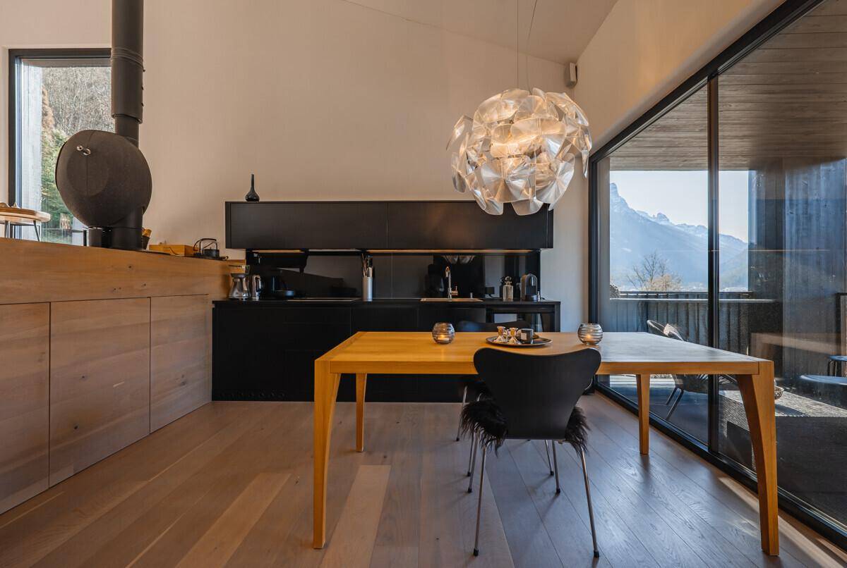 Heller Essbereich mit Holztisch, moderner Küche und großen Fenstern mit Bergblick, sehr einladend.