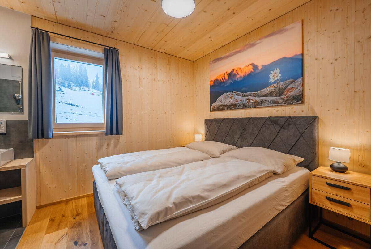 Gemütliches Schlafzimmer mit Doppelbett, Holzvertäfelung und malerischem Blick auf die verschneiten Berge.