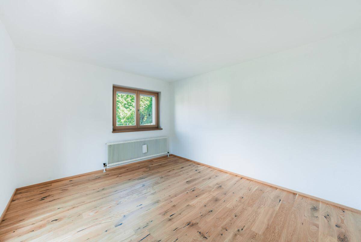 Leeres Zimmer mit Holzboden und Fenster, das viel natürliches Licht hereinlässt.